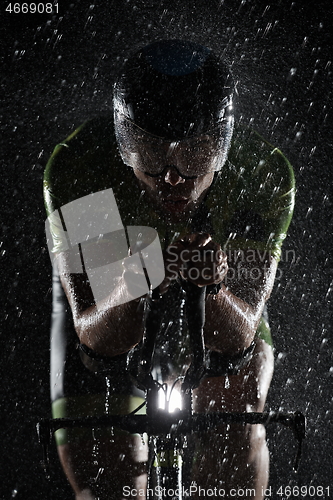 Image of triathlon athlete riding bike fast on rainy night