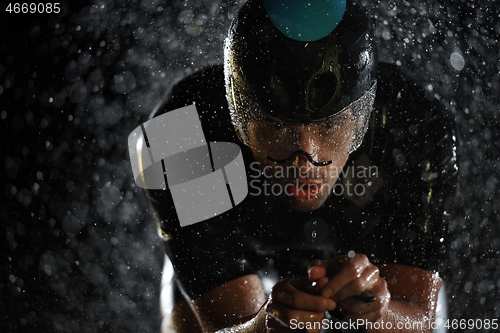 Image of triathlon athlete riding bike fast on rainy night