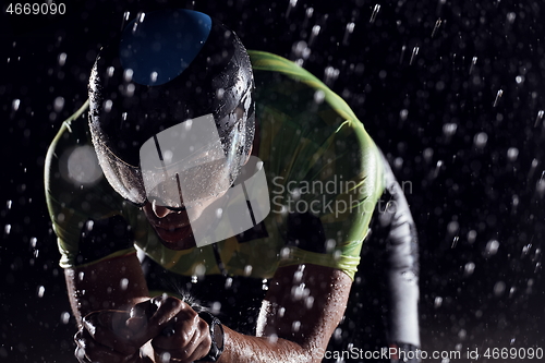 Image of triathlon athlete riding bike fast on rainy night