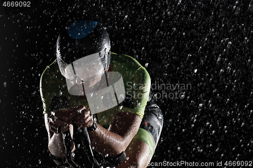 Image of triathlon athlete riding bike fast on rainy night