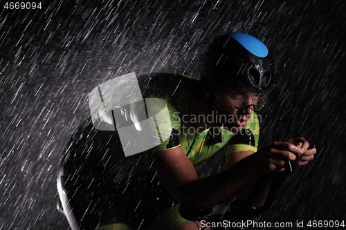 Image of triathlon athlete riding bike fast on rainy night