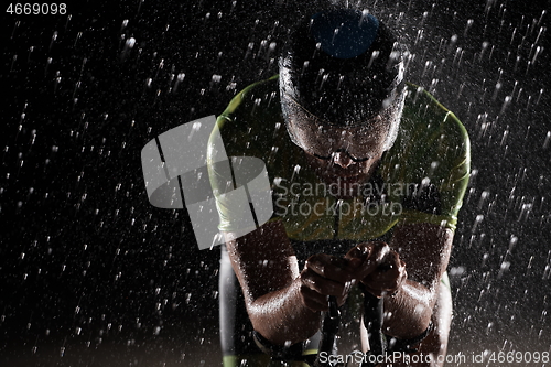 Image of triathlon athlete riding bike fast on rainy night