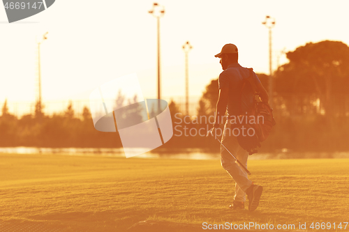 Image of golfer  walking and carrying golf  bag at beautiful sunset