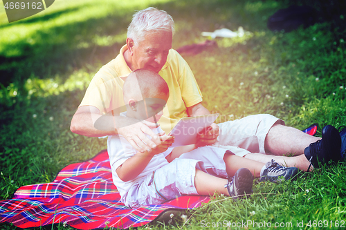 Image of grandfather and child in park using tablet