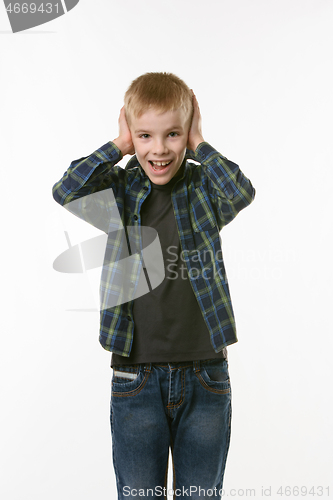 Image of The boy covers his ears with his hands and shouts looking into the frame against a white background