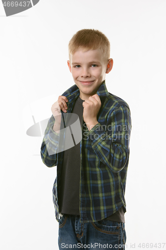 Image of blond boy on a white background holds hands behind the collar of a checkered shirt