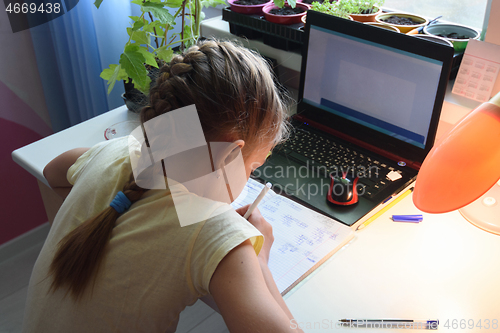 Image of Girl solves math examples in notebook in front of laptop