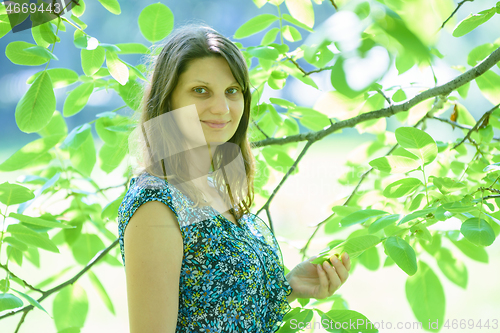 Image of Girl smiles against a branch with green leaves in sunny weather