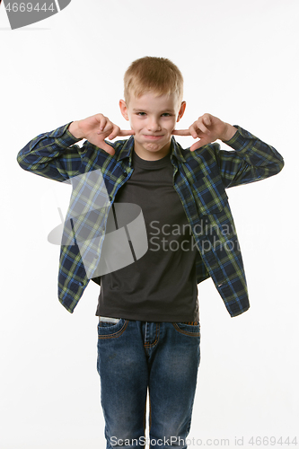 Image of boy on a white background in a plaid shirt blows his cheeks with his fingers