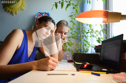 Image of Mother solves daughter\'s assignments to study in notebooks at home at the desk