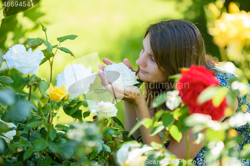 Image of Young girl enjoys the scent of roses in the park