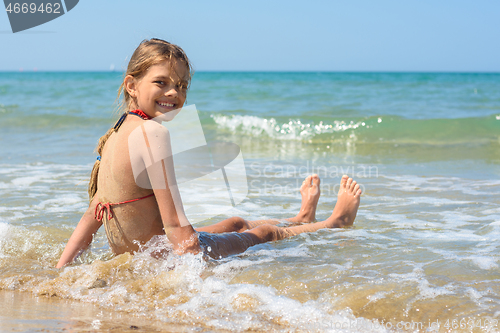 Image of Happy girl sitting on a sandy beach and looking back smiling looked into the frame