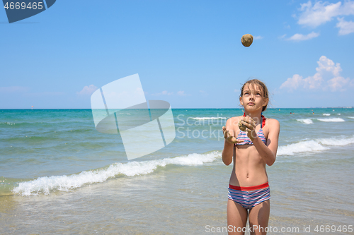 Image of A girl of ten years juggles sand balls on the seashore