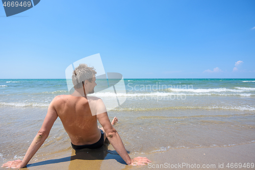 Image of A man sits on the seashore and looks into the distance