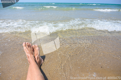 Image of Feet of a man on a sandy beach, in the background a sea surf and horizon