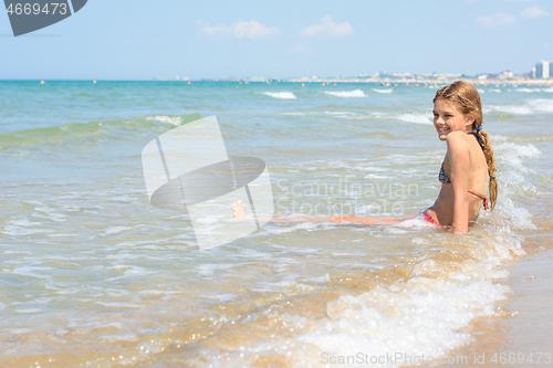 Image of A girl of ten years old sits in the water on an empty seashore