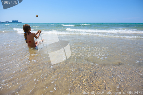 Image of Girl sitting on the seashore and throws sand balls