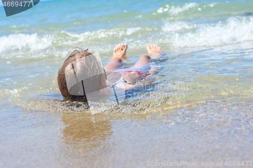 Image of A girl lies on her back in shallow water on the sea sandy coast