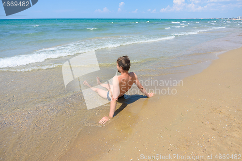 Image of A man sits on an empty sandy sea beach in the water