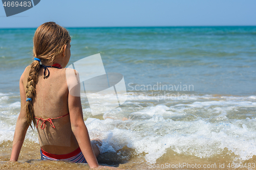 Image of A girl sits on a sandy sea beach and looks into the distance