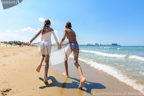 Image of Two girls run along the a beach