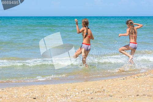 Image of Two sisters run into the sea on a hot sunny day