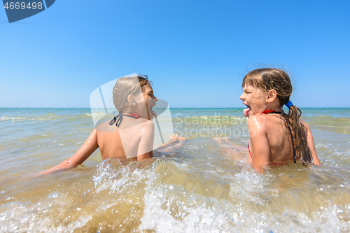 Image of Children sit together in shallow water and show each other tongue