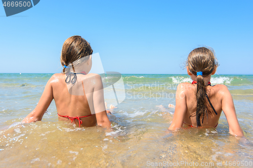 Image of Children sit in the water on the coast and look into the distance