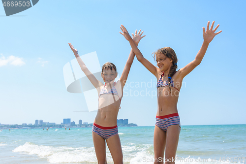 Image of Two girls joyfully raised their hands up on the sea on vacation and swimming