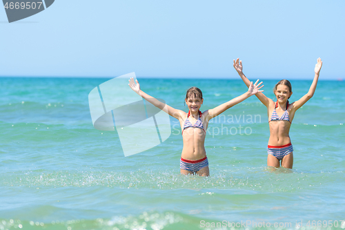 Image of Children stand in sea water and joyfully raise their hands up