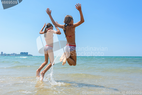 Image of Two girls joyfully bounce on the seashore