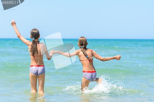Image of Sisters joyfully and happily run into the sea on a hot sunny day