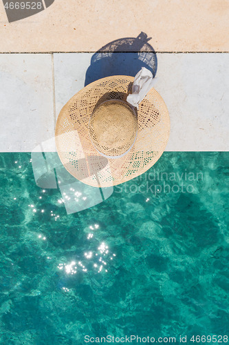 Image of Woman wearing big summer sun hat relaxing on pier by clear turquoise sea.