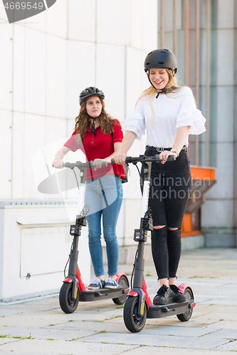 Image of Trendy fashinable teenager girls riding public rental electric scooters in urban city environment. New eco-friendly modern public city transport in Ljubljana, Slovenia