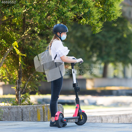 Image of Trendy fashinable teenager girl wearing corona virus protective face mask in public while using rental electric scooters in city environment. New eco-friendly city transport in Ljubljana, Slovenia