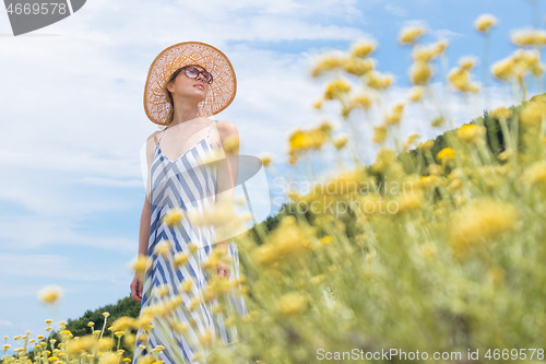 Image of Young woman wearing striped summer dress and straw hat standing in super bloom of wildflowers, relaxing while enjoing beautiful nature of of Adriatic sea coastal nature of Croatia.