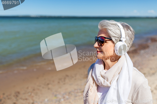 Image of old woman in headphones listens to music on beach