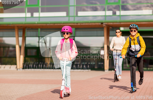 Image of happy school children with mother riding scooters