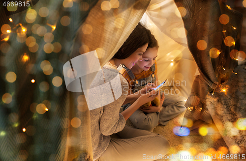 Image of happy family with smartphone in kids tent at home