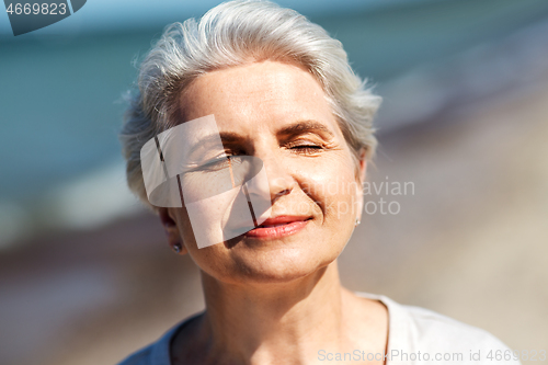 Image of portrait of senior woman enjoying sun on beach