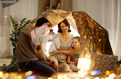 Image of happy family playing in kids tent at night at home