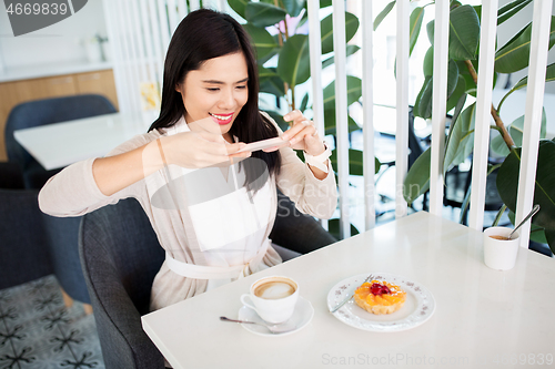 Image of woman photographing coffee by smartphone at cafe