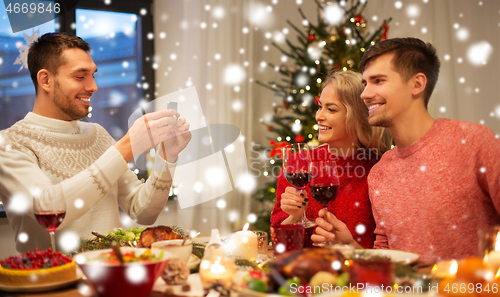 Image of happy friends photographing at christmas dinner