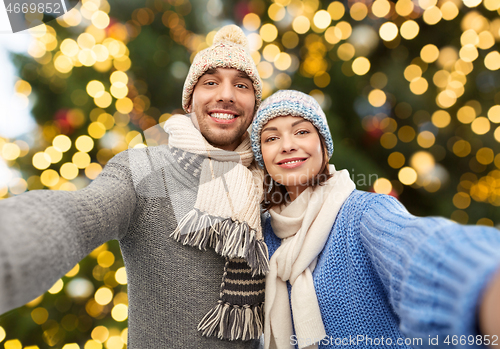 Image of happy couple taking selfie over christmas lights