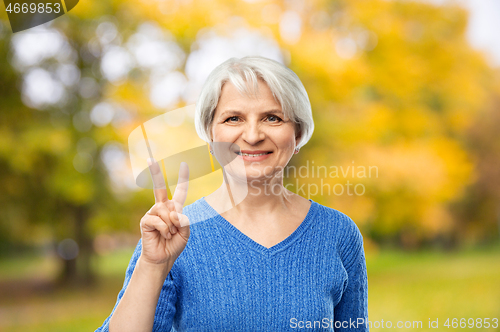 Image of senior woman showing peace in autumn park