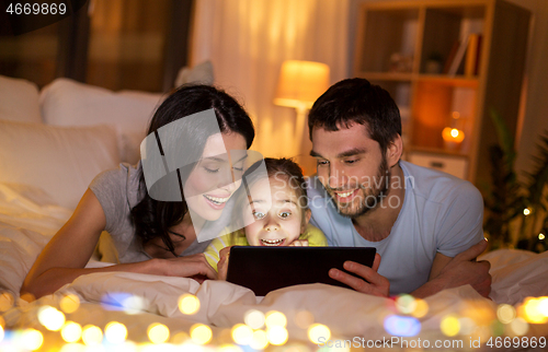 Image of family with tablet pc in bed at night at home