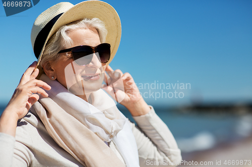 Image of happy senior woman in sunglasses and hat on beach