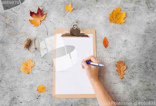 Image of hand writing on white paper on clipboard in autumn