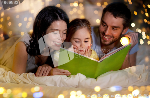 Image of happy family reading book in bed at night at home