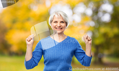 Image of happy old woman celebrating success in autumn park